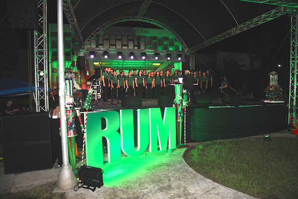Foto del coro de cámara durante el tradicional evento de la Navidad Colegial. El grupo está en el escenario, de frente las letras del RUM iluminadas en color verde.