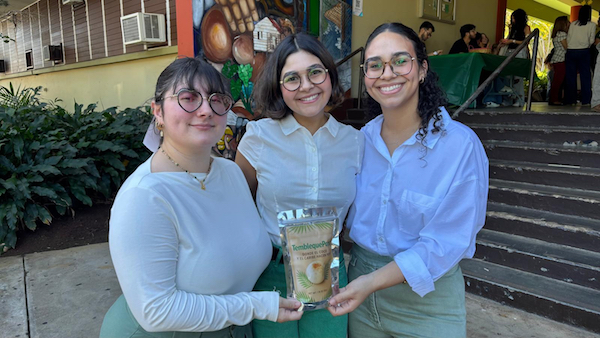 Las estudiantes de maestría en Ciencia y Tecnología de Alimentos: Alexandra Shields Cruz, Nancelys M. Rodríguez Oquendo y Nicole Rodríguez Trujillo obtuvieron el Primer lugar del curso CITA 6603 y el Premio de Innovación, originalidad y mejor presentación, por sus Tembleque Pops, en la más reciente edición de la Competencia de productos nuevos. Las tres de pie frente al edificio Piñero posan con su producto.