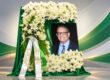 Foto de Johnny Flores enmarcada en una letra C del Colegio de Mayagüez y rodeada de flores blancas con unas cintas en el homenaje póstumo.