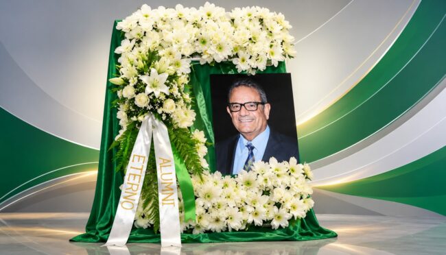 Johnny Foto de Johnny Flores enmarcada en una letra C del Colegio de Mayagüez y rodeada de flores blancas con unas cintas en el homenaje póstumo.