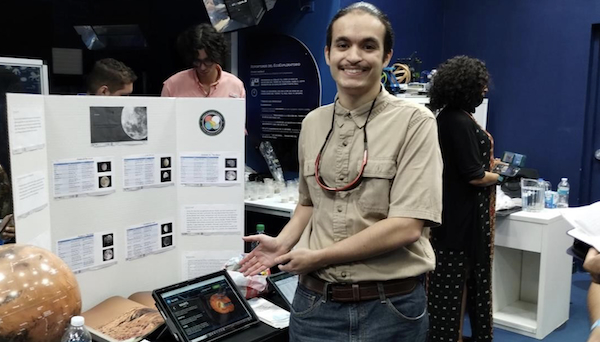 Chris M. Justiniano Vélez, quien recién culminó su maestría en el Departamento de Geología del RUM, obtuvo la prestigiosa beca Huel D. Perkins que otorga la Universidad del Estado de Louisiana para apoyar a los estudiantes en su carrera doctoral en esa institución. En la foto, frente a un cartel de exhibición de planetas cuando formó parte de un voluntariado en el EcoExploratorio en 2023.