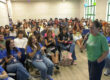 Una exalumna colegial se dirige a un grupo de recién admitidos al Recinto Universitario de Mayagüez (RUM), de pie, al centro y los estudiantes sentados la observan.