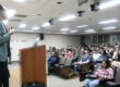 Uno de los recursos invitados se dirige de pie desde el podio a los estudiantes recién admitidos a los programas de maestría y doctorado en su bienvenida al Recinto Universitario de Mayagüez.