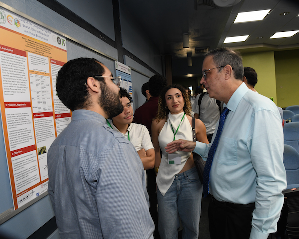 El doctor Raúl E. Torres Muñiz, coordinador del Programa de Afiliados a la Industria, conversa con un grupo de estudiantes durante la más reciente reunión. Todos de pie, frente al afiche de investigación grupal.