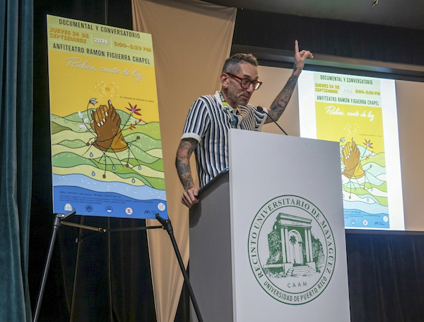 El documentalista del Laboratorio de Historia Oral, Guillermo Gómez Álvarez se dirige al público desde el podio en el anfiteatro Figueroa Chapel. A su espalda, el cartel del documental en color amarillo.
